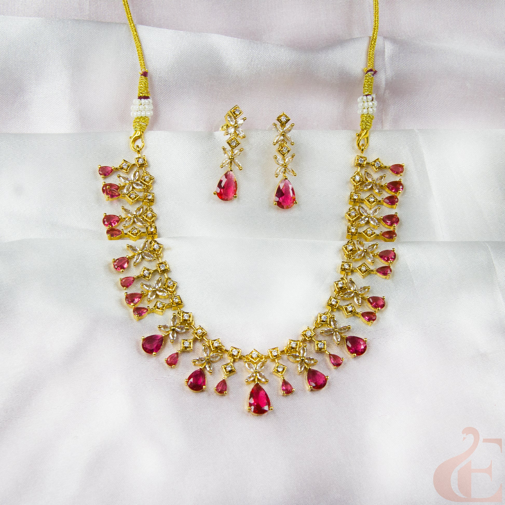 Gold necklace with red gemstones and matching earrings on a white background